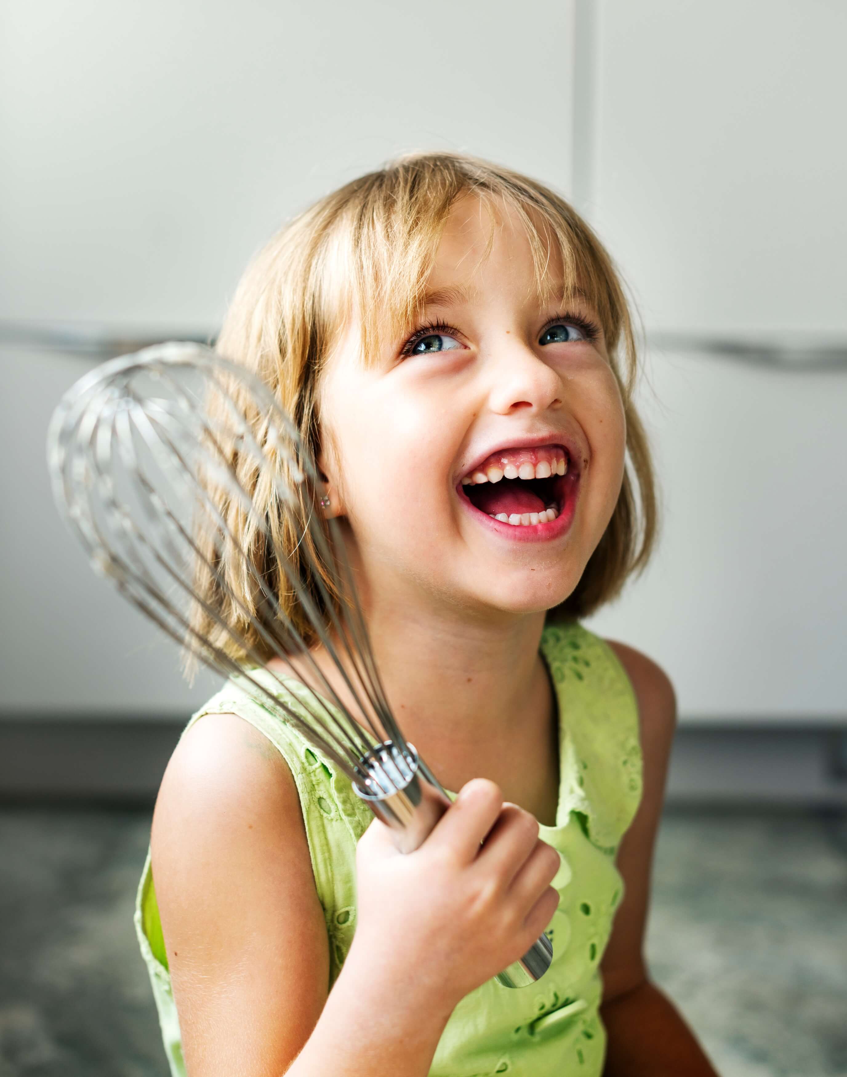 A little girl chef holding a mixing spatula while laughing. 