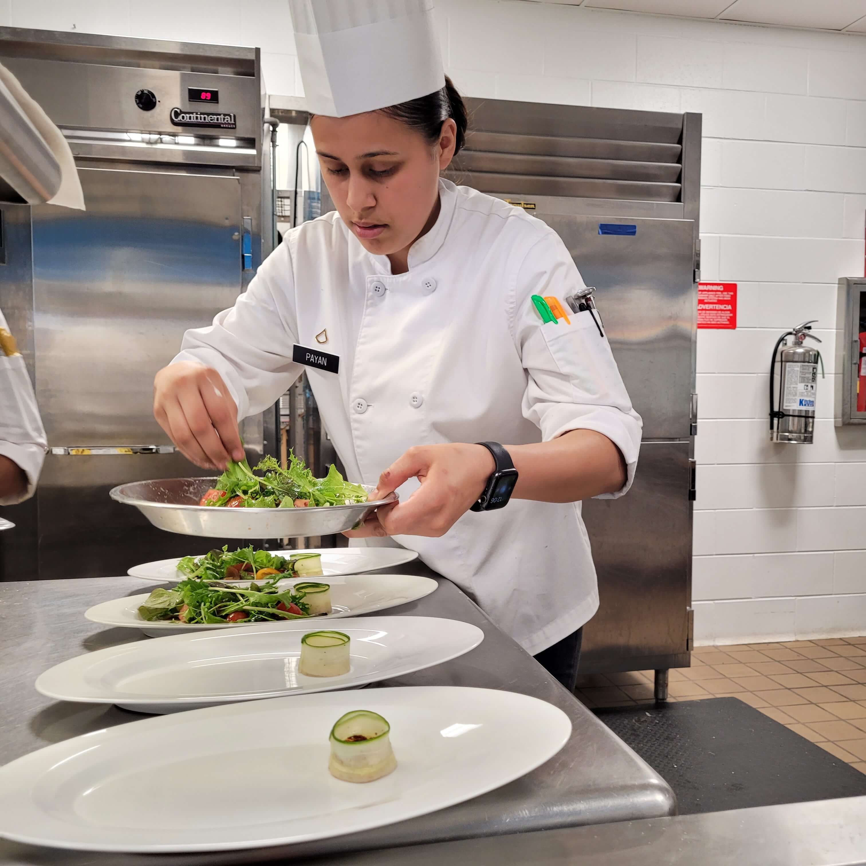 An adult female chef portioning vegetables to dishes.