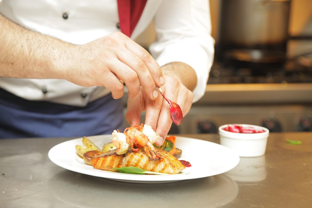 Two hands adding sauces to a prepared meal on a table.