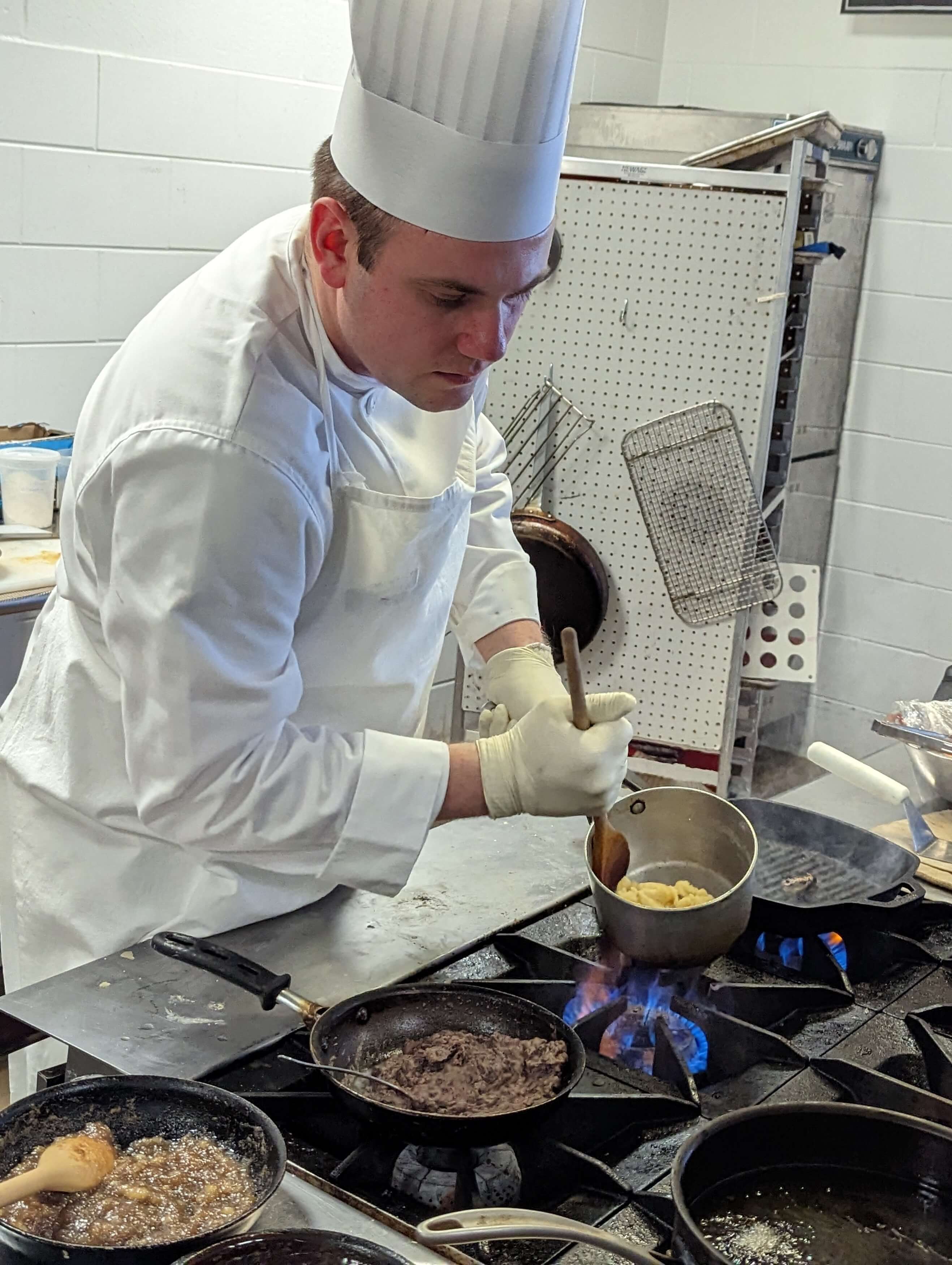 A male chef dressed in full chef's costume cooking on a stove.